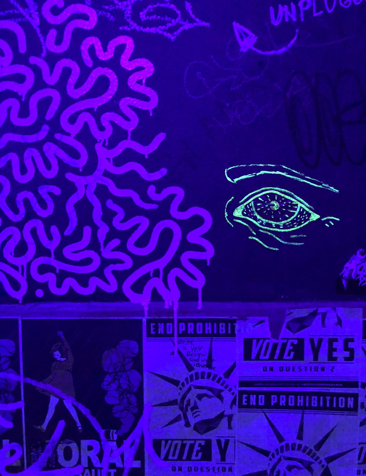 A green eye and pink drawings glowing on the Madhouse bathroom wall